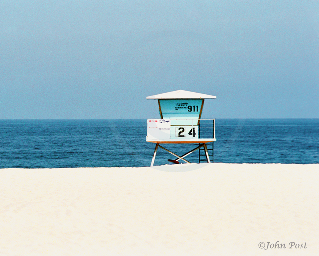 Lifeguard tower on beach, clear  sky with volleyball net and seagull on top of pole.