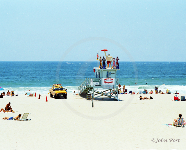 Lifeguard tower on beach, clear sunset sky with volleyball net and seagull on top of pole.