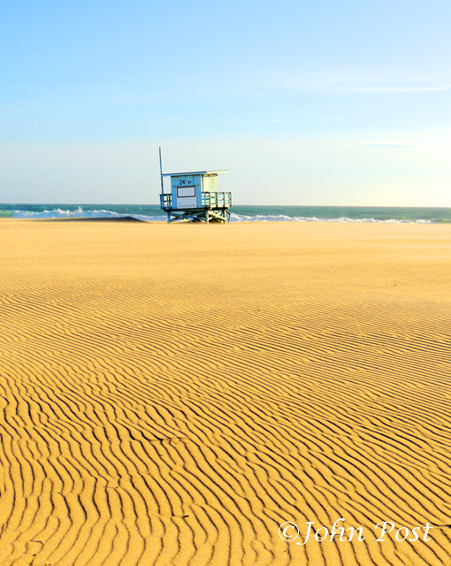 Lifeguard tower on beach, clear sunset sky with volleyball net and seagull on top of pole.
