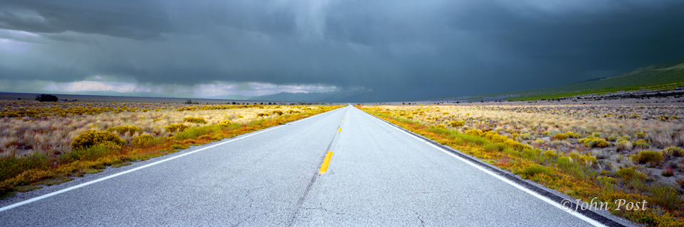 View down straight road leading into Great Sand Dunes National Park, Colo.Storm clouds in sky
